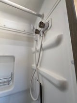 This clean white shower in an RV rental features a handheld showerhead, faucet, shower rod, and a small metal shelf.