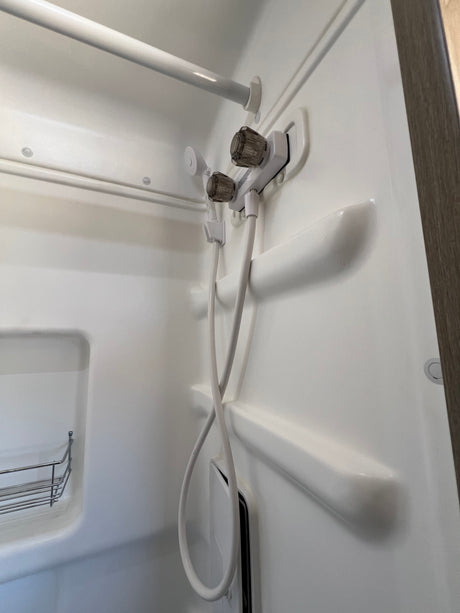 This clean white shower in an RV rental features a handheld showerhead, faucet, shower rod, and a small metal shelf.