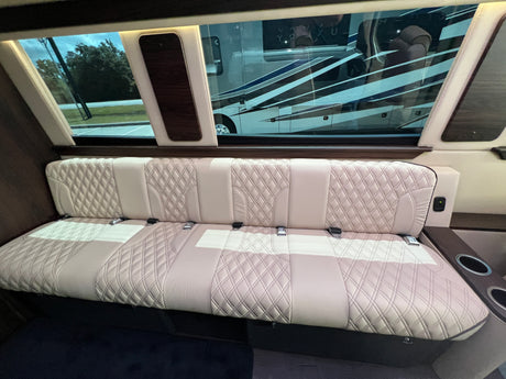 Inside a luxury RV rental: cream quilted leather bench seat with seatbelts, large windows reflecting another RV.