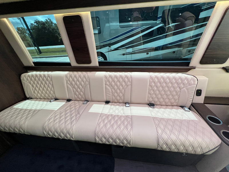 Inside a luxury RV rental: cream quilted leather bench seat with seatbelts, large windows reflecting another RV. — photo 7