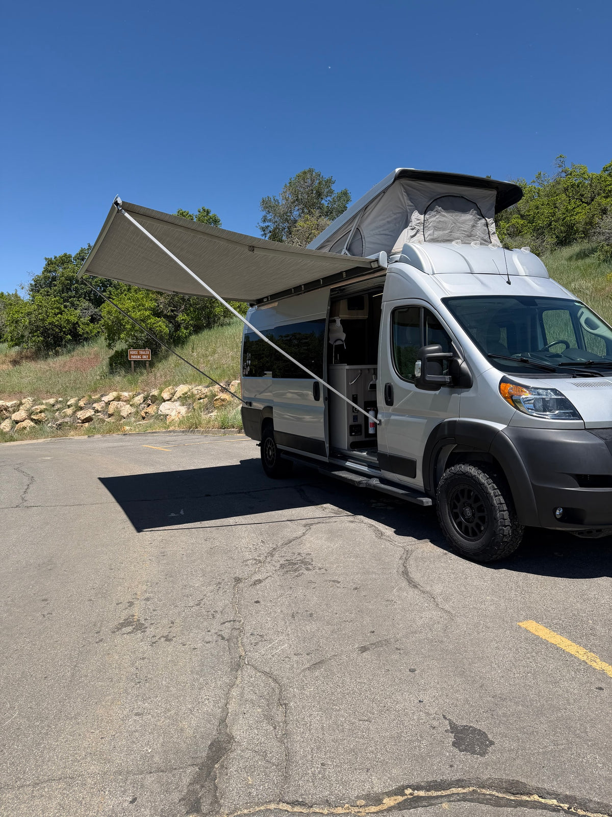 Explore with this RV rental! Silver campervan with pop-top and awning out, parked in a scenic spot. — photo 3