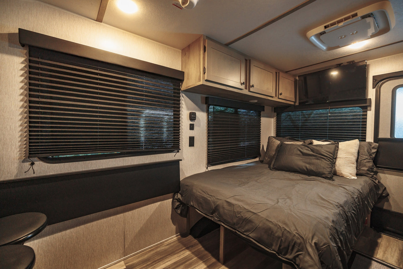 RV rental bedroom: dark bed, pleated blinds, overhead cabinets, wall-mounted TV, and ceiling AC unit for comfort. — photo 20