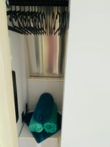Compact RV rental closet: black hangers on a rod, with neatly rolled blue and green towels on a shelf.