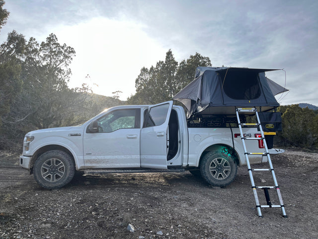 White Ford F-150 truck with rooftop tent & ladder, ready for outdoor adventure. A unique RV rental option.