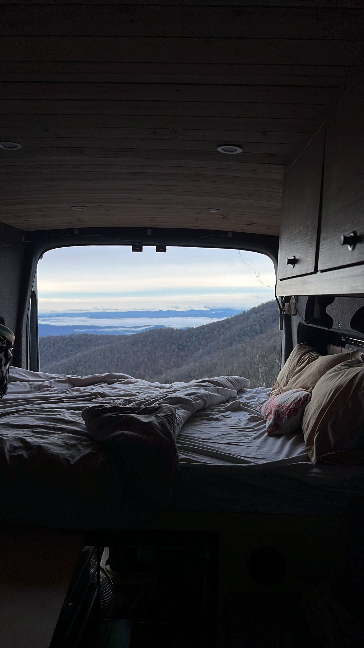 **RV rental** adventure: Cozy van bed with a stunning mountain view and misty peaks from the open back.