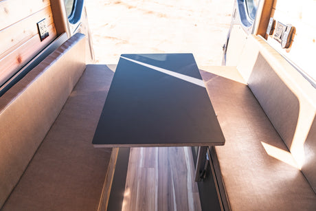 Modern RV rental interior: sleek table, comfy bench seating, wood paneling, and power for your next adventure.