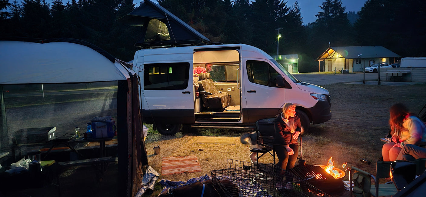A cozy evening with an RV rental camper van, pop-top tent open, and friends by the campfire at a busy campground. Classic van life.