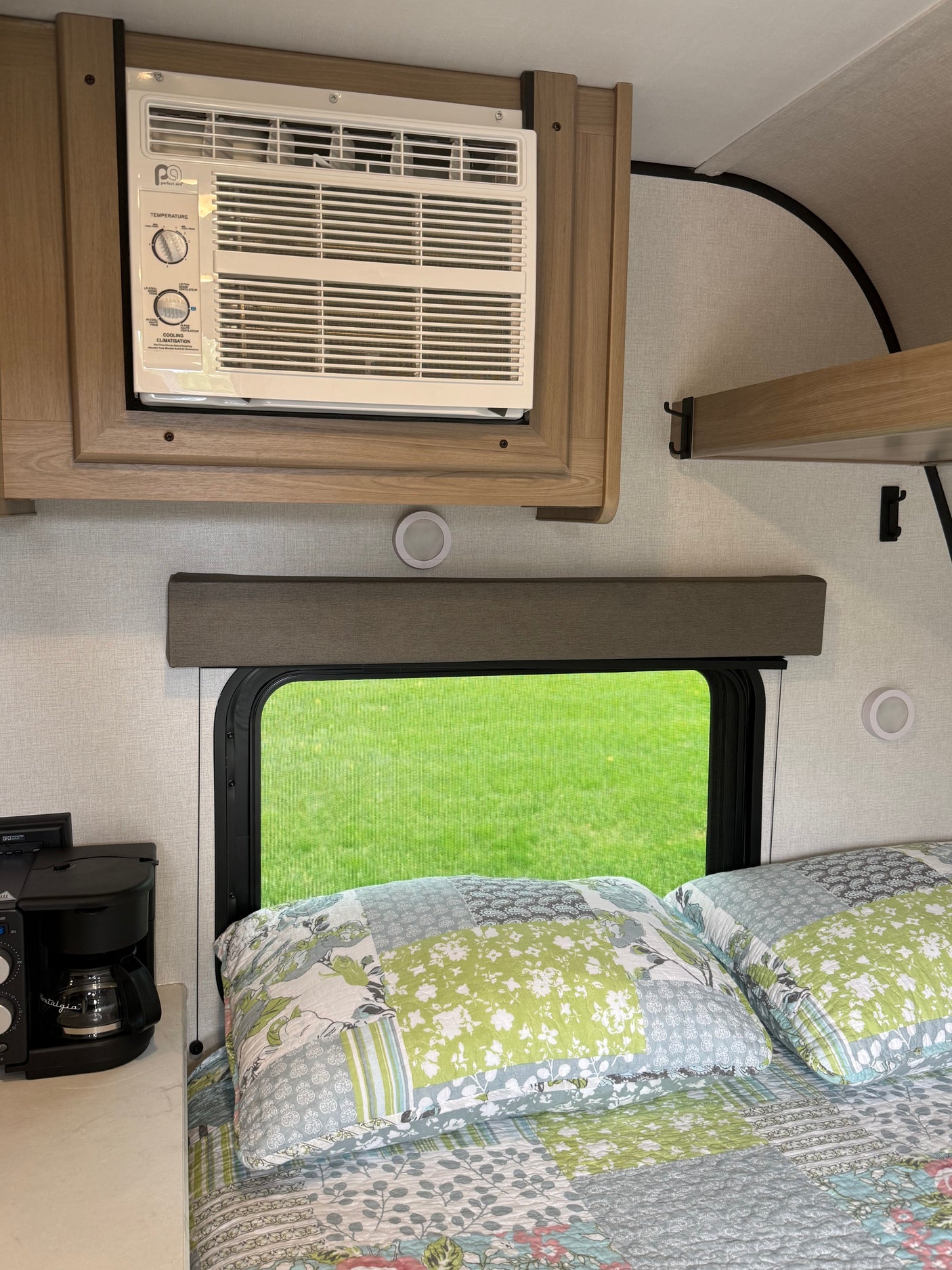 Cozy RV rental bedroom featuring an AC unit mounted above a window with a green grass view, and a coffee maker.