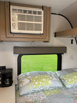 Cozy RV rental bedroom featuring an AC unit mounted above a window with a green grass view, and a coffee maker.