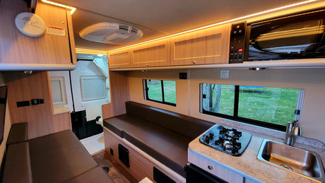 Bright RV rental interior showing a kitchen, seating area, overhead cabinets, and a compact bathroom. Ideal for road trips.