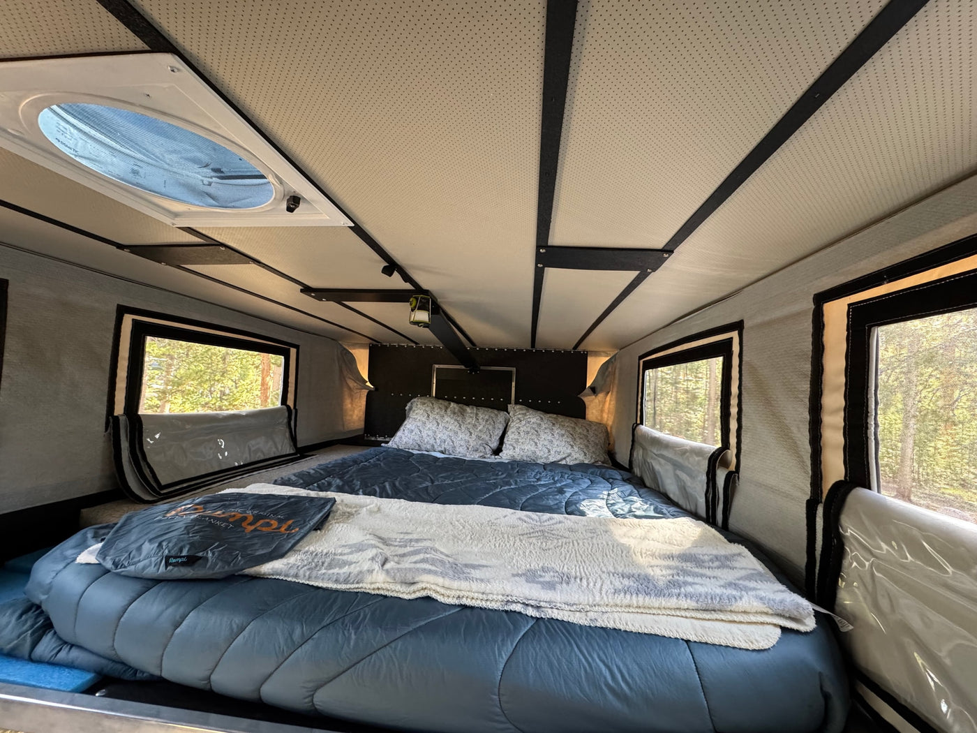 Inside a comfortable RV rental bedroom, featuring a large bed, side windows with tree views, and a Dometic ceiling vent. — photo 4