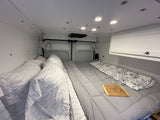 Inside an RV rental: a plush camper van bedroom with ambient lighting, fans, and a cozy bed for comfortable travel.