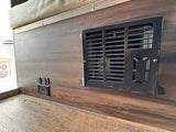 An RV rental interior shows a black furnace vent, USB ports, and electrical outlets on a wood-grain panel.