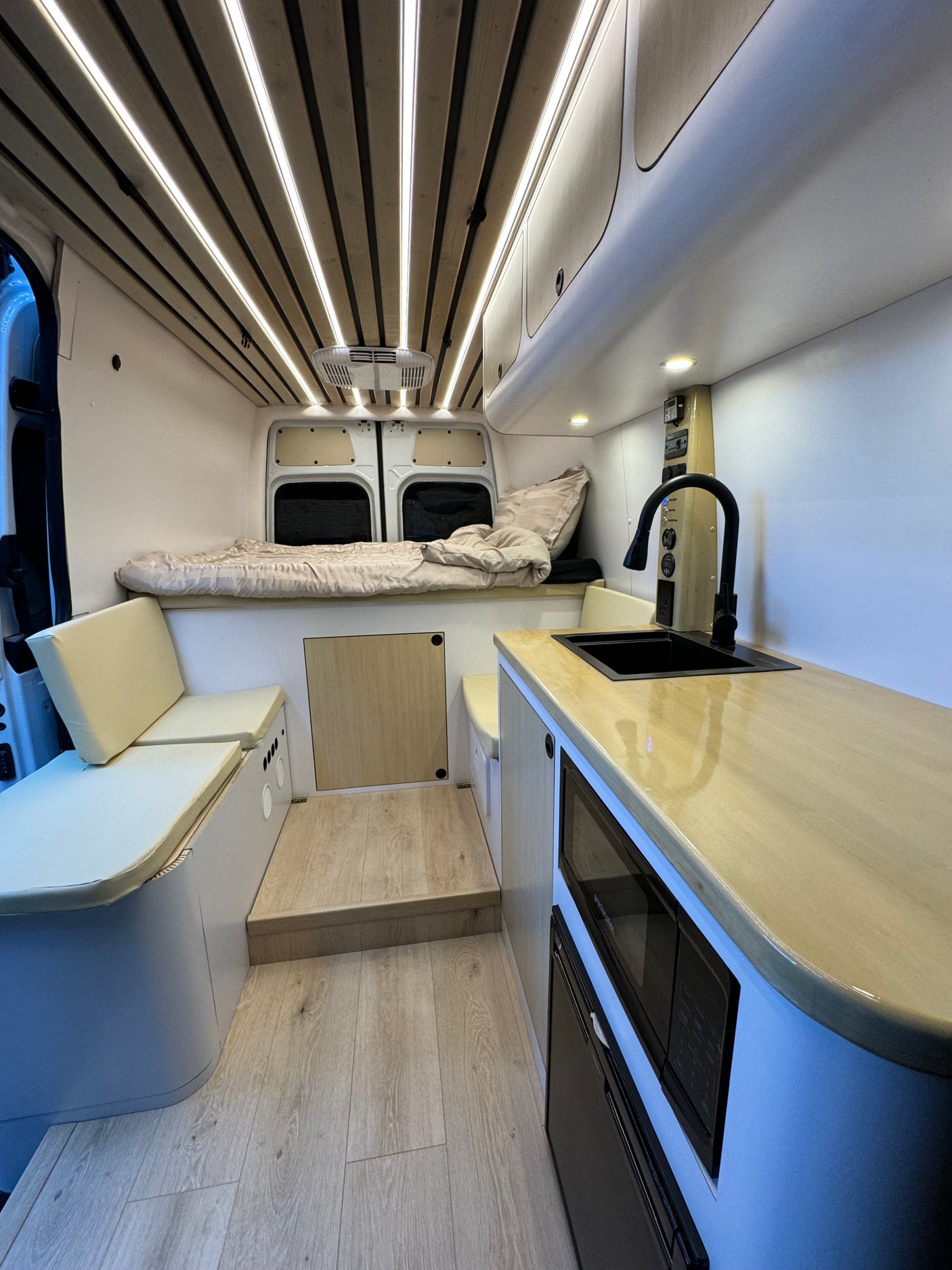 RV rental: Modern camper van interior featuring a bed, kitchen with sink/appliances, and comfortable seating.