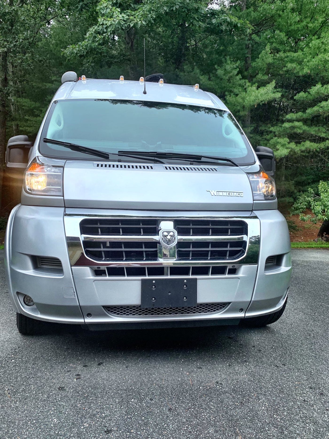 Front view of a sleek silver Winnebago RV rental van. Parked outdoors on asphalt with green trees. — photo 20
