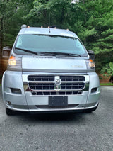 Front view of a sleek silver Winnebago RV rental van. Parked outdoors on asphalt with green trees.