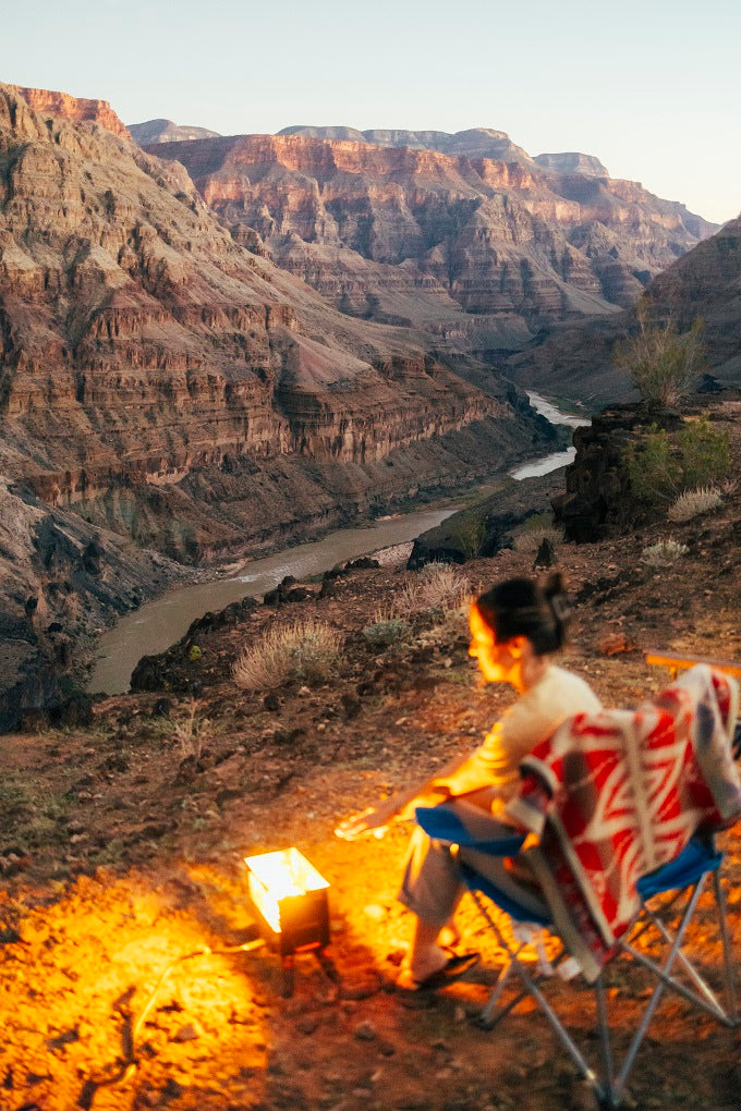 Evening glow in a canyon with a river below. A person sits by a fire in a chair, perfect for an rv rental trip.