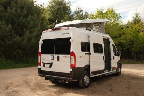 Rear view of a white Winnebago Solis pop-top camper van, ideal for your next RV rental adventure in nature.