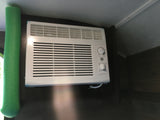 White GE air conditioner with control knobs and green foam insulation, seen inside an RV rental for cooling comfort.