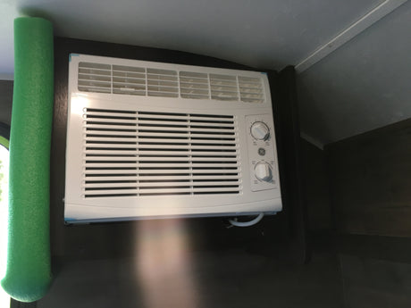 White GE air conditioner with control knobs and green foam insulation, seen inside an RV rental for cooling comfort.