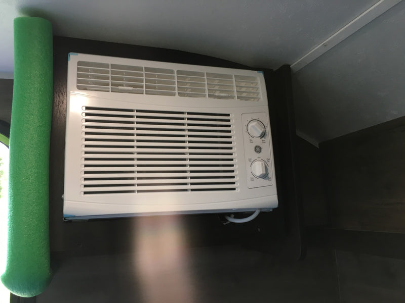 White GE air conditioner with control knobs and green foam insulation, seen inside an RV rental for cooling comfort. — photo 7