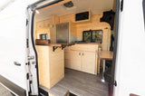 Bright, wood-paneled RV rental interior showcasing a compact kitchen, fridge, and dining setup for comfortable mobile living.