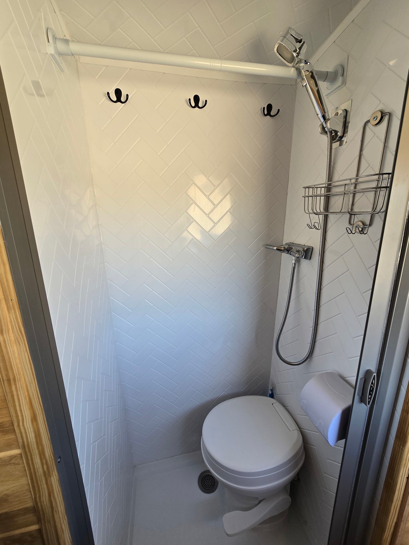 Compact RV rental wet bath featuring a shower, toilet, and convenient hanging hooks in a white herringbone tile design.