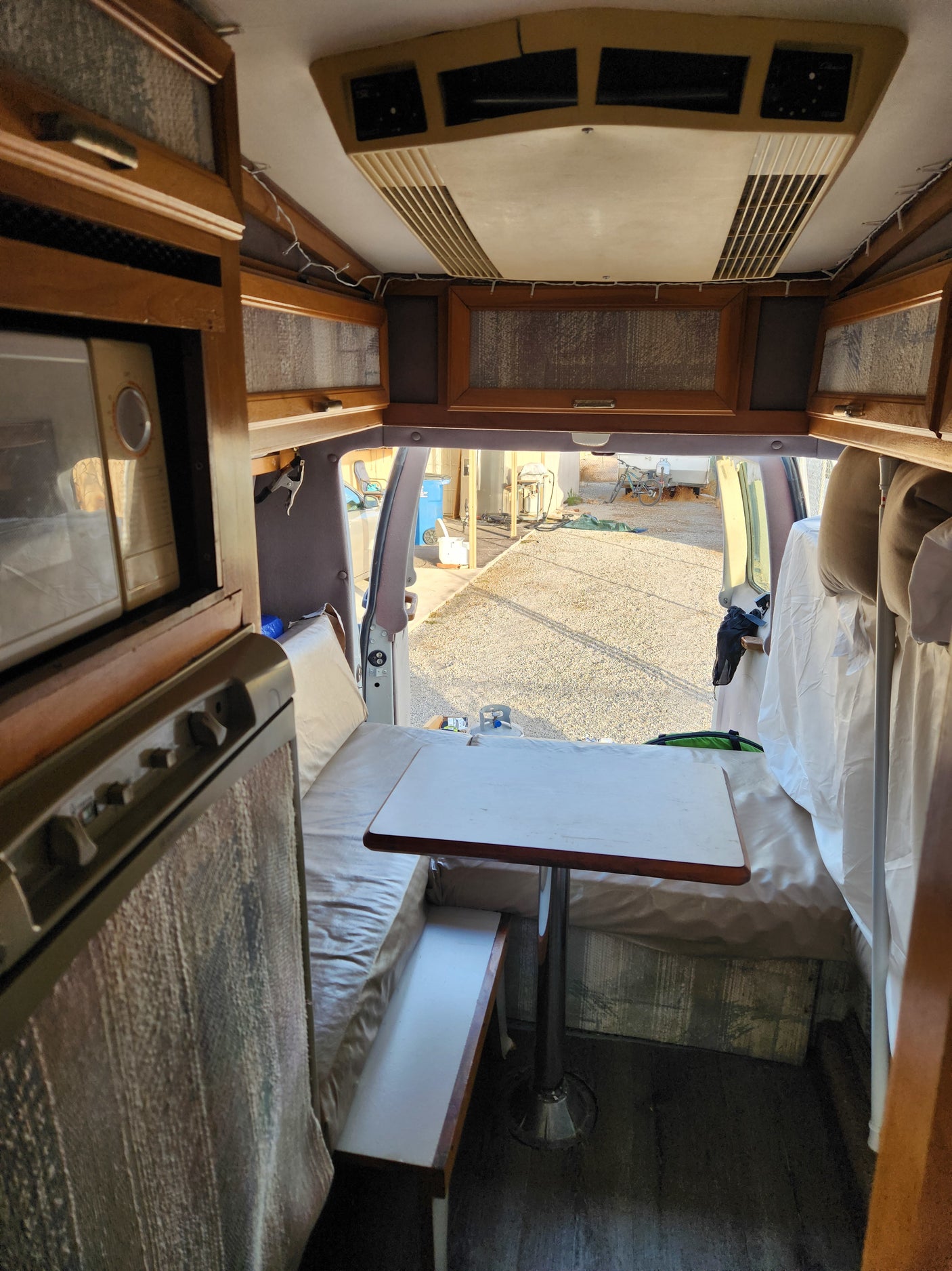 Inside a compact RV rental, showcasing a functional living area with a microwave, dining table, bench seating, and AC.