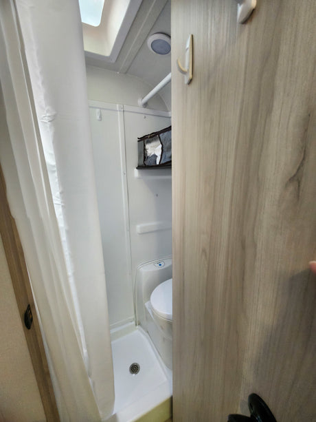 Compact RV rental wet bath, combining shower and toilet for efficient use of space, with hooks and storage.