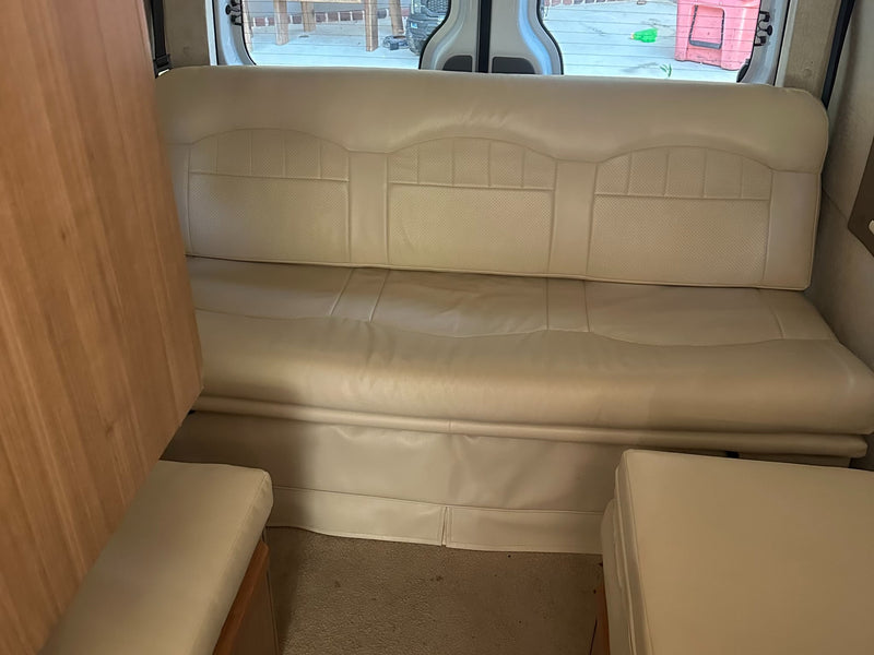  revealing a kitchenette and comfortable seating for your travel adventures.|Compact RV rental kitchen with open two-burner stove and sink on a speckled countertop.|Compact RV rental wet bath with toilet paper on the toilet — photo 7