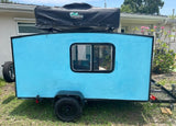 This blue teardrop camper, featuring a roof-top tent & spare tire, is perfect for an RV rental outdoor trip.