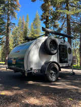 Teardrop RV rental parked in a sunny forest setting, ideal for outdoor adventures and camping trips.