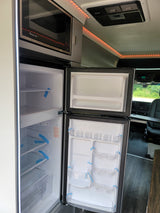 RV rental kitchen: Open dual-door refrigerator, microwave oven, and ceiling lights. Ready for travel!
