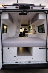 This rv rental showcases a modern camper van interior with a bed, under-bed storage, overhead cabinets, and a compact kitchenette.