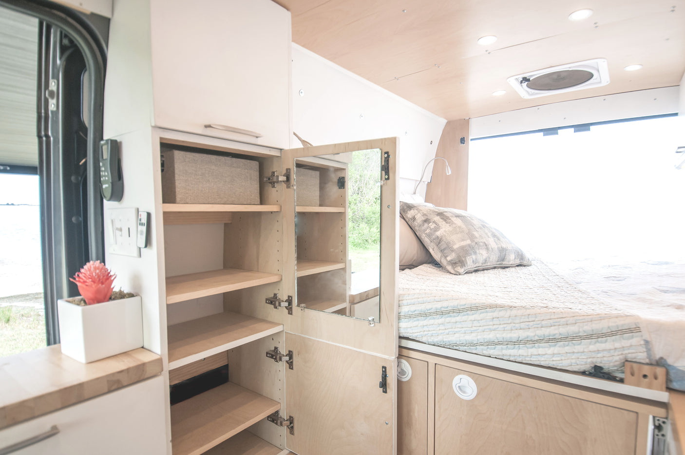 Cozy RV rental interior: Bed with storage, compact kitchen counter, and open cabinet system for efficient living.
