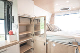 Cozy RV rental interior: Bed with storage, compact kitchen counter, and open cabinet system for efficient living.