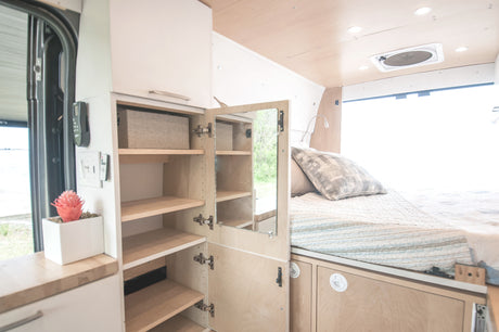 Cozy RV rental interior: Bed with storage, compact kitchen counter, and open cabinet system for efficient living.