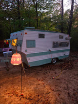 Enjoy a cozy evening in a vintage RV rental. This retro camper is nestled in a forest, illuminated by a glowing lantern.