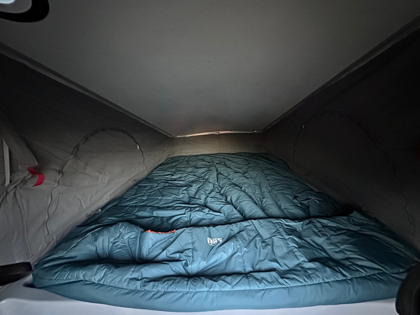 Pop-top RV rental bed with a large, teal sleeping bag. Ready for a comfortable camping adventure.