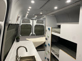 This bright RV rental interior features a kitchen sink, rear bed, and bunk beds with playful climbing holds for a unique family travel experience.