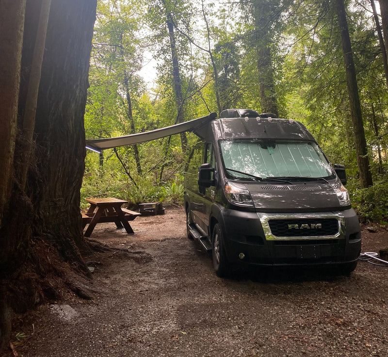 An RV rental is parked at a forest campsite with an extended awning — photo 1
