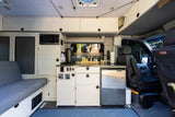 RV rental interior: organized kitchen with microwave, fridge, sink, ample cabinets, and a side lounge bed.