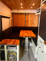 Inside an RV rental: Warm wooden interior, L-shaped seating, dining table, and built-in shelving for a cozy living space.