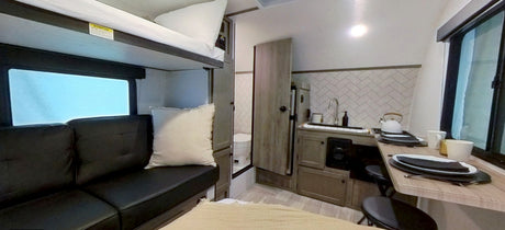 RV rental interior featuring bunk beds, a compact kitchen, dining area, and a sofa for travel.