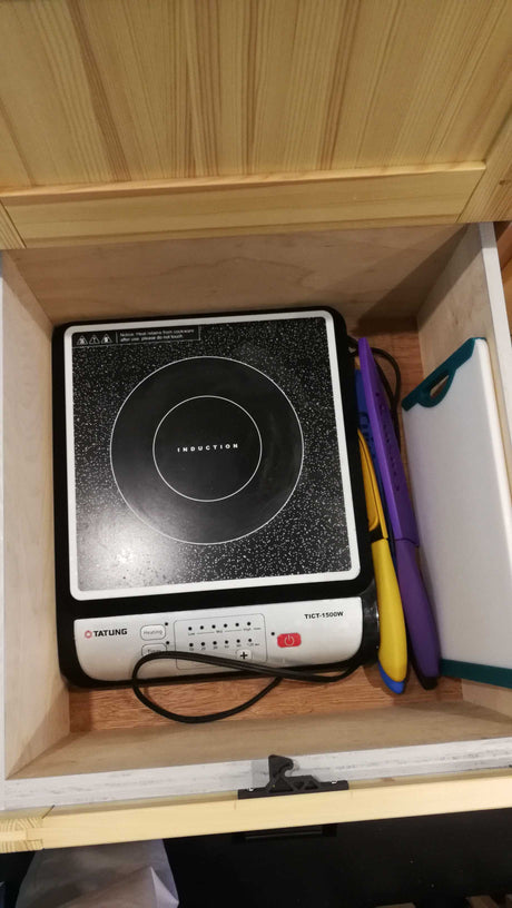 Compact kitchen essentials: induction cooktop, knives, and cutting board, neatly stored in an RV rental drawer.