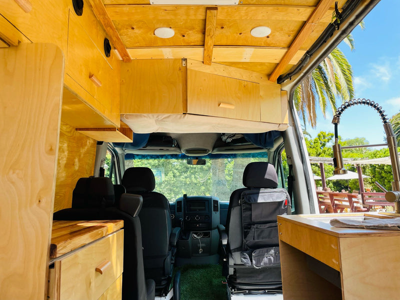 Bright rv rental interior of a custom camper van, featuring wooden cabinets, a kitchen sink, and front seats. — photo 18