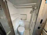 Compact rv rental bathroom: a white molded shower stall with a toilet, showerhead, and small wire shelf, designed for efficiency.