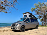 Explore Hawaii with this RV rental! A pop-top camper van on a sandy beach next to the ocean under a blue sky.