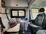 RV rental interior: cozy camper van dining area with white quilted seating, table, and controls.