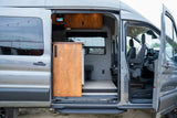 RV rental: See inside a modern camper van conversion with an open side door, showcasing its kitchen, control panel, & comfy seating.